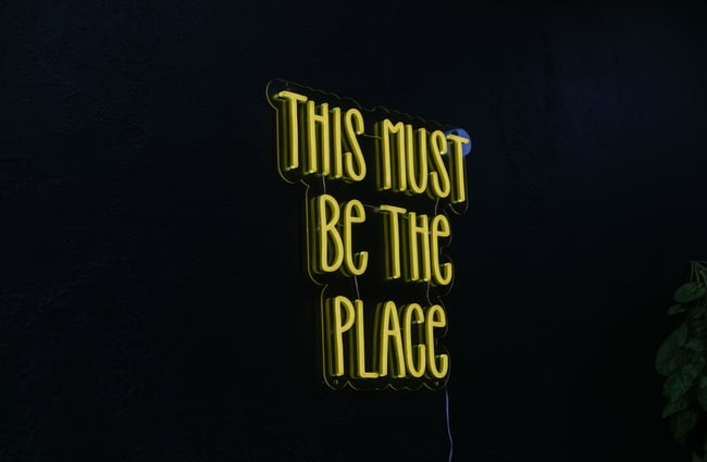 A close up of a neon yellow sign that says 'this must be the place'.