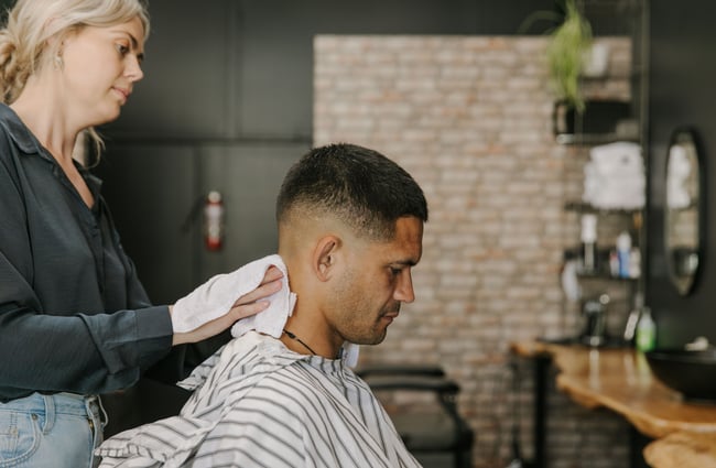 A close up of a man receiving a hair cut from a female barber.