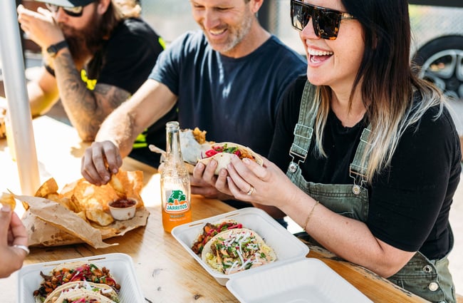 People smiling as they enjoy corn chips and tacos from Burrito Craft.