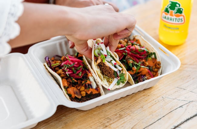 A hand reaching for the middle of three tacos in a box.