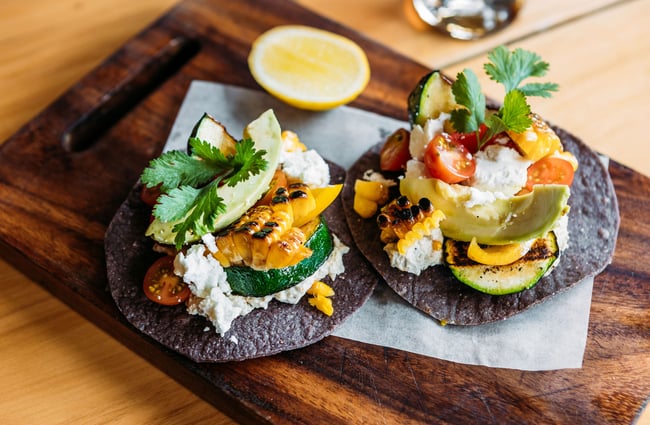 Two vegetarian tostadas, on black corn taco shells, on a wooden board with a slice of lemon at Cardrona Hotel.