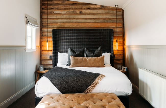 Inside a bedroom at Cardrona Hotel with a tall, black headboard against a horizontal timber-lined wall.