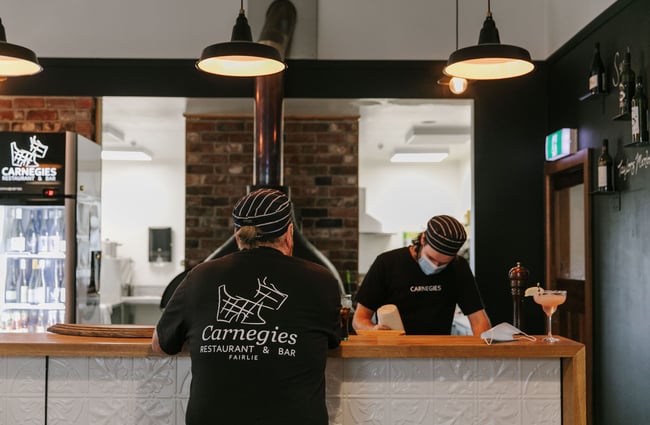 Person standing at the counter wearing a branded Carnegie's Restaurant and Bar t-shirt.