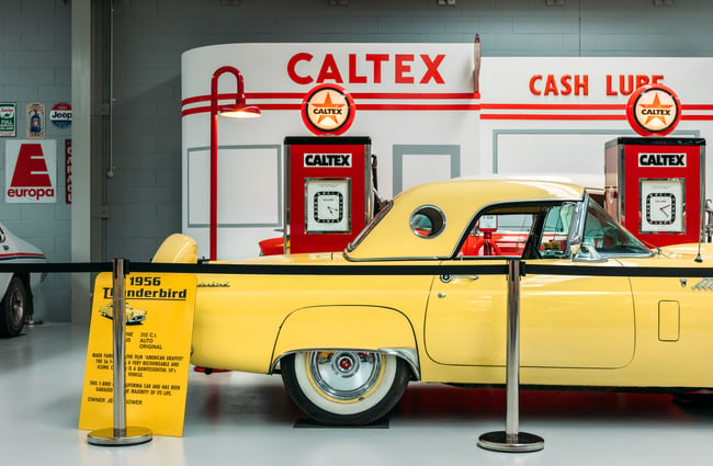 A close up of a yellow car in front of a Caltex sign.