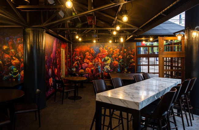 A colourful mural on a wall providing a backdrop to the high dining tables and chairs.