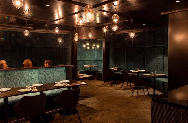 A black and blue-green velvet interior of a darkly lit restaurant.