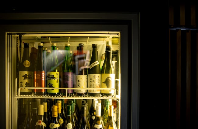 A close up of bottles of sake in a darkly lit fridge.