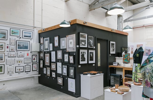 A black wall inside the CRAFTED workshop covered in framed art prints.