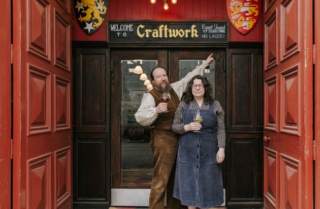 The owners of the Craftwork Brewery standing in the entry way holding brew each.