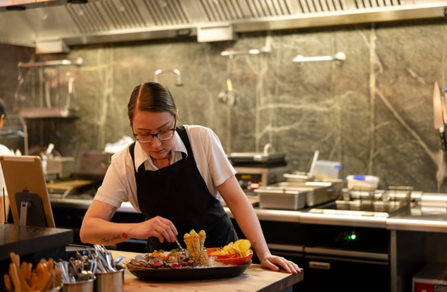 A staff member plating a meal in a restaurant kitchen.
