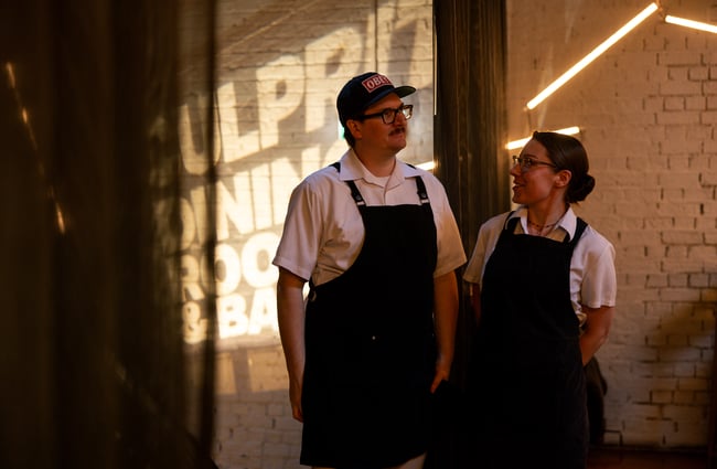 A man and woman wearing aprons looking at each other.