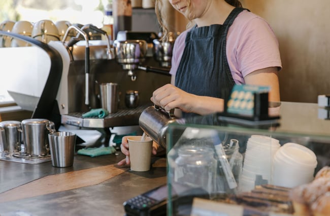 A barista from Curbside, pouring milk into the coffee takeaway cup.