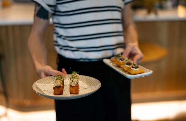 Waiter holding two elegant plates of Mediterranean-inspired food at Earl