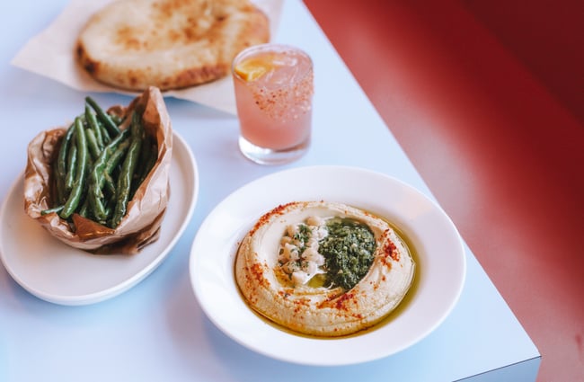 A plate of green beans and a plate of hummus on a table.