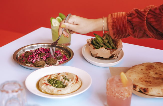 A hand holding a fork reaching for a piece of falafel on a plate.