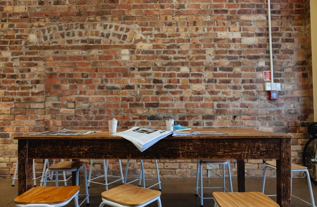 Wooden table inside by a brick wall.