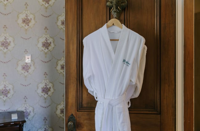 A white robe hanging on a wooden door inside a hotel room.