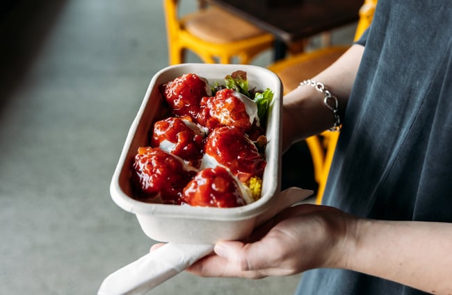 Hands holding a box of meatballs covered in sauce.