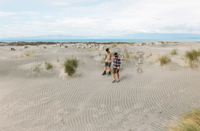Two men wearing hats walking on the sandy dunes.