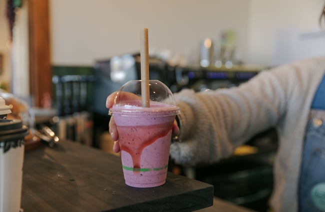A hand holding a pink smoothie.