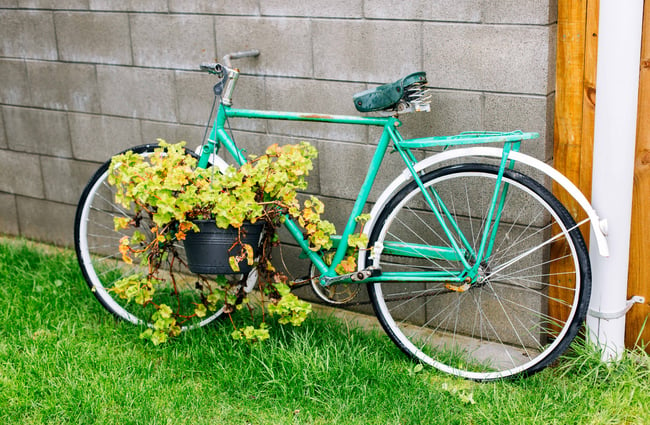 An old green bike covered in flowers leaning up against a brick wall.