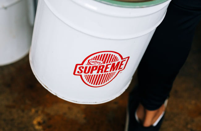 A person carrying a large bucket of Coffee Supreme coffee beans inside Gispy Kitchen cafe Wellington.