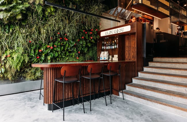 Entrance of Glou Glou with living plant wall, bar leaner and stools, and a few concrete stairs leading into main dining area