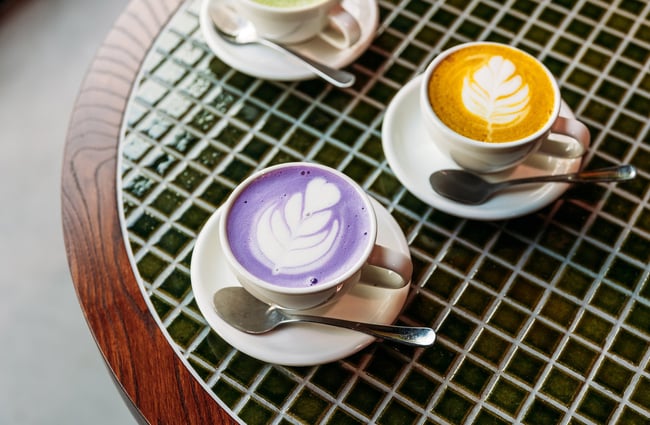 Ube latte and turmeric latte on a green tiled tabletop