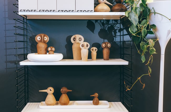 Wooden owls on display on floating walls against a dark blue wall.