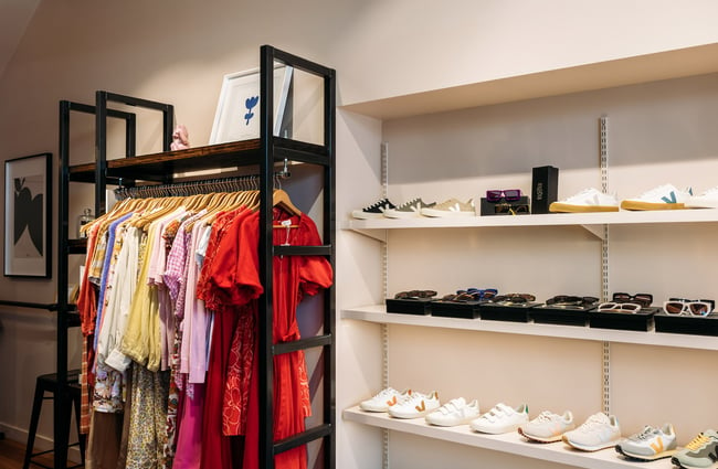 Interior of clothing store with Veja shoes on shelf and bright clothes hanging on racks