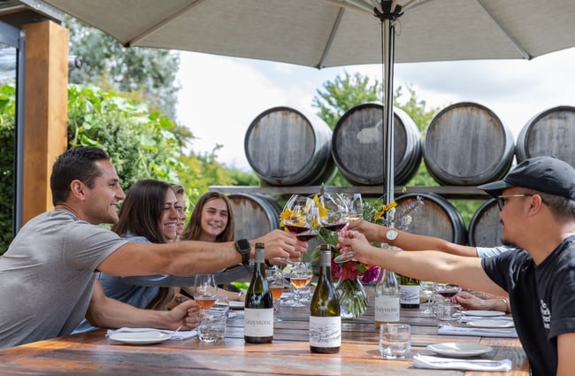 A group of people seated at an outdoor table raise their filled wine glasses together in cheers at Greystone Wines.