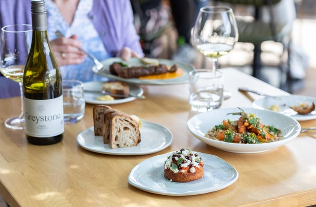 A plate of bread, other prepared dishes, wine and water glasses and a bottle of Greystone Chardonnay on a dining table at Greystone Wines.