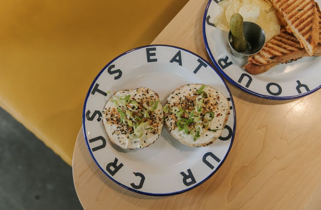 Bagel spread with cream cheese, spring onion and seeds on an enamel plate at Grizzly Baked Goods in the Christchurch CBD.