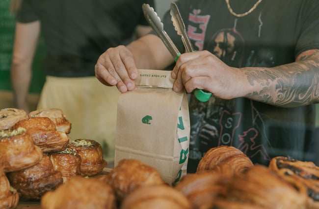 Close up of pastries and a staff member folding closed a paper takeaway bread bag at Grizzly Baked Goods in the Christchurch CBD.
