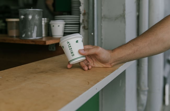 A hand holding a takeaway Grizzly coffee cup at Grizzly Baked Goods in the Christchurch CBD.