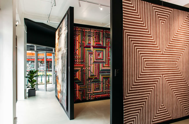 Large multi coloured rugs on display against large black walls.