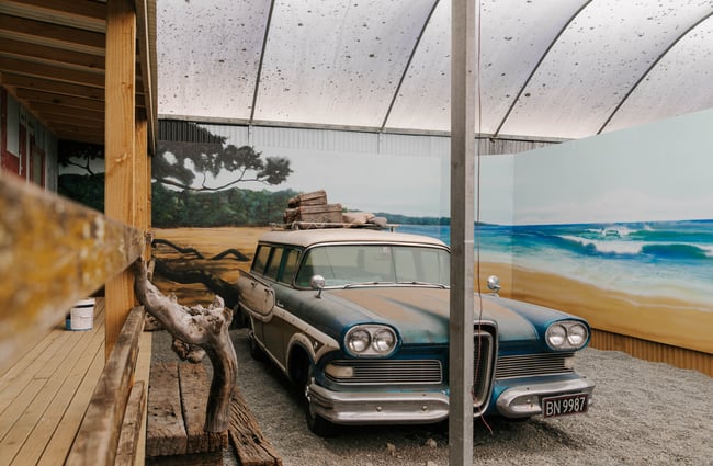 Classic car parked with a painted beach mural behind.