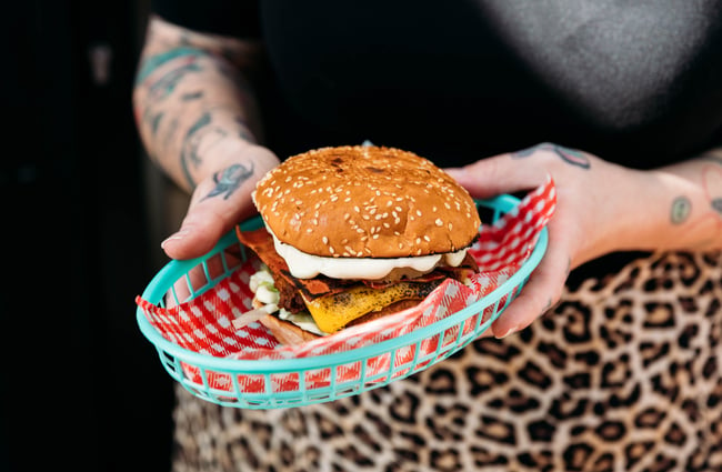 A staff member holding a burger in a plastic bowl.