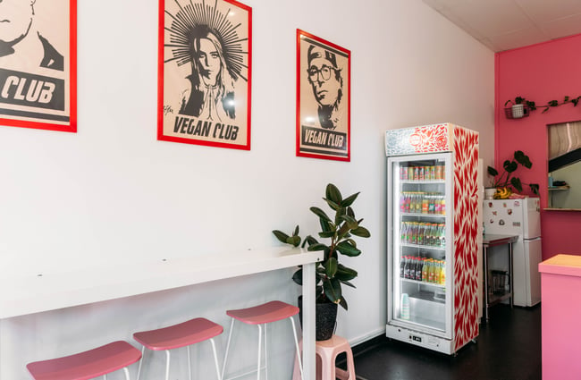 A drinks fridge and high seats in a white and pink painted cafe.