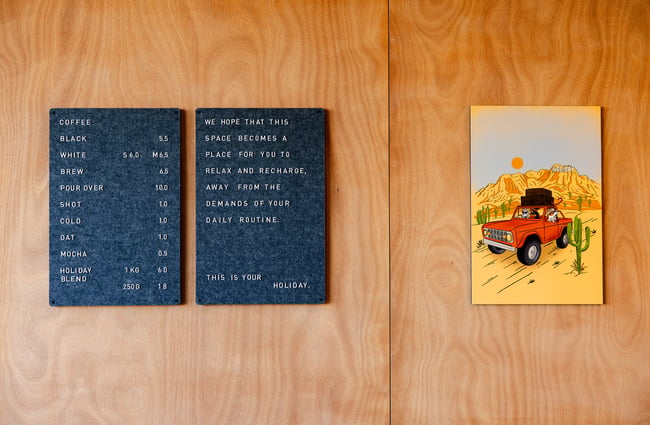 Coffee menu on timber wall at Holiday cafe with bright vacation-inspired artwork next to it