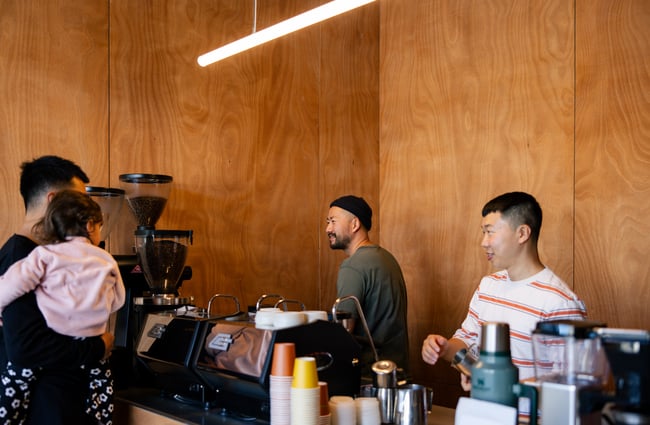 Two baristas smiling behind counter and serving man holding his daughter