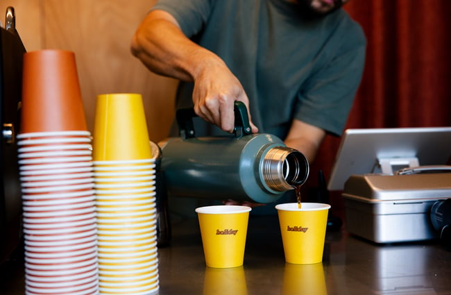 Barista pouring filter coffee into Holiday branded takeaway cups