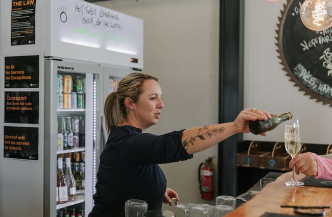 Lady in a black top pouring a glass of wine from behind the counter.