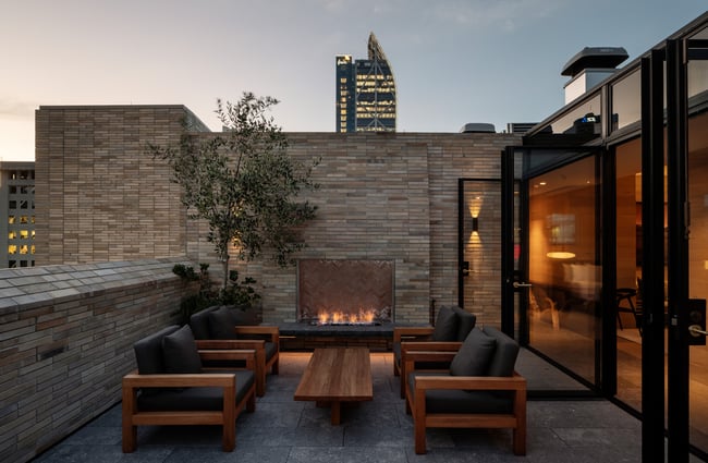 A fireplace next to tables and chairs on the roof of Hotel Britomart at dusk.