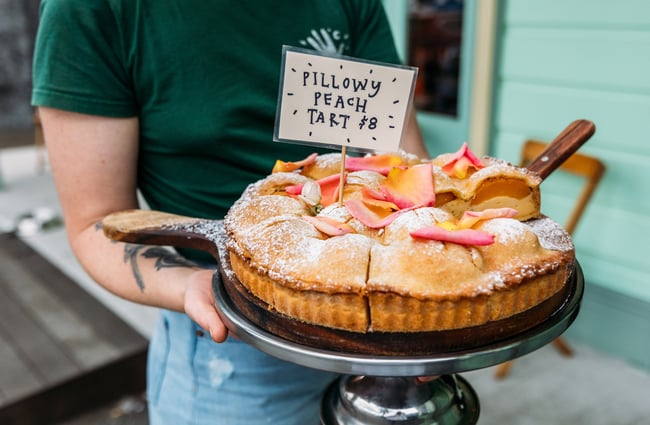 Someone holding plate of cake with sign sticking out saying "pillowy peach cake"