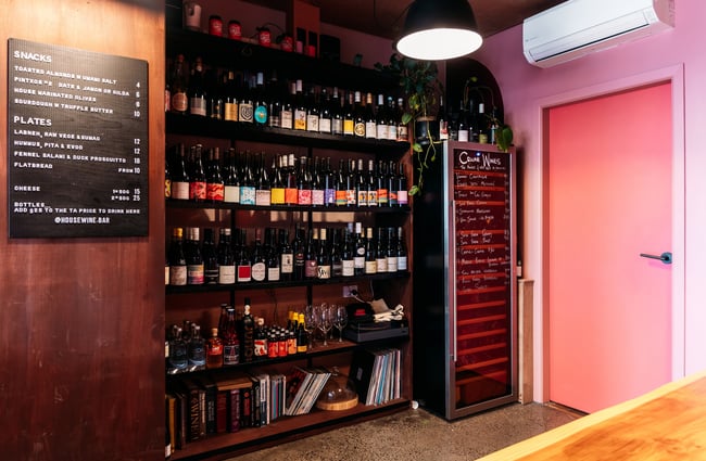 Wine bottles on shelves by a pink door.