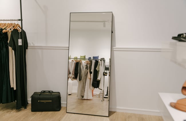 A large mirror sit against a white wall showing a reflection of the inside of the store.