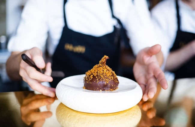 A chef places a plate with a chocolate covered, pumpkin-shaped dessert on the counter at Inati.