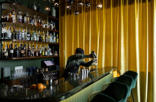A bartender pours a cocktail at Inati's green marbled bar top.