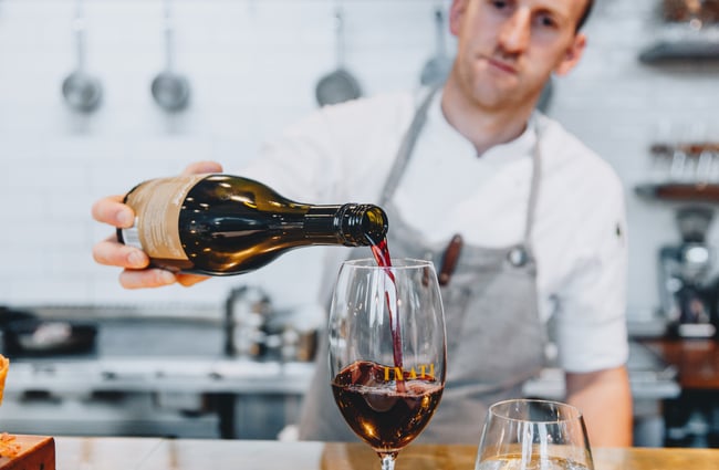 Wine being poured into a glass by a chef inside Inati restaurant Christchurch, New Zealand.